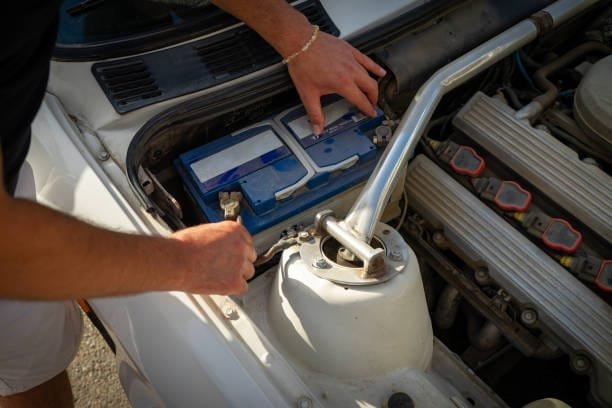 Car not working in summer, young man checking battery, top view