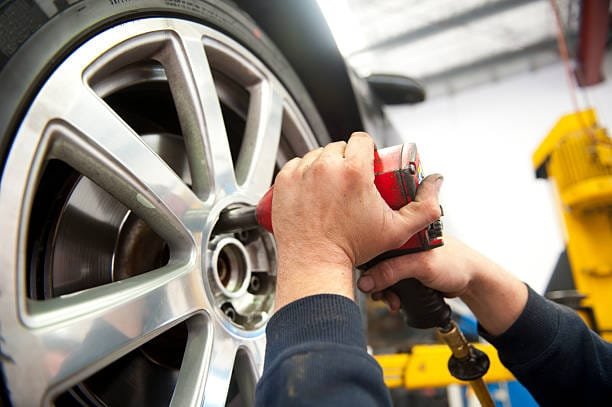 Detail image of mechanic hands with tool, changing tyre of car, with blurred background of garage.