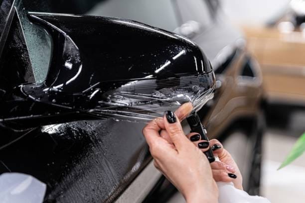 Car detailing technician applying transparent ppf foil on car body